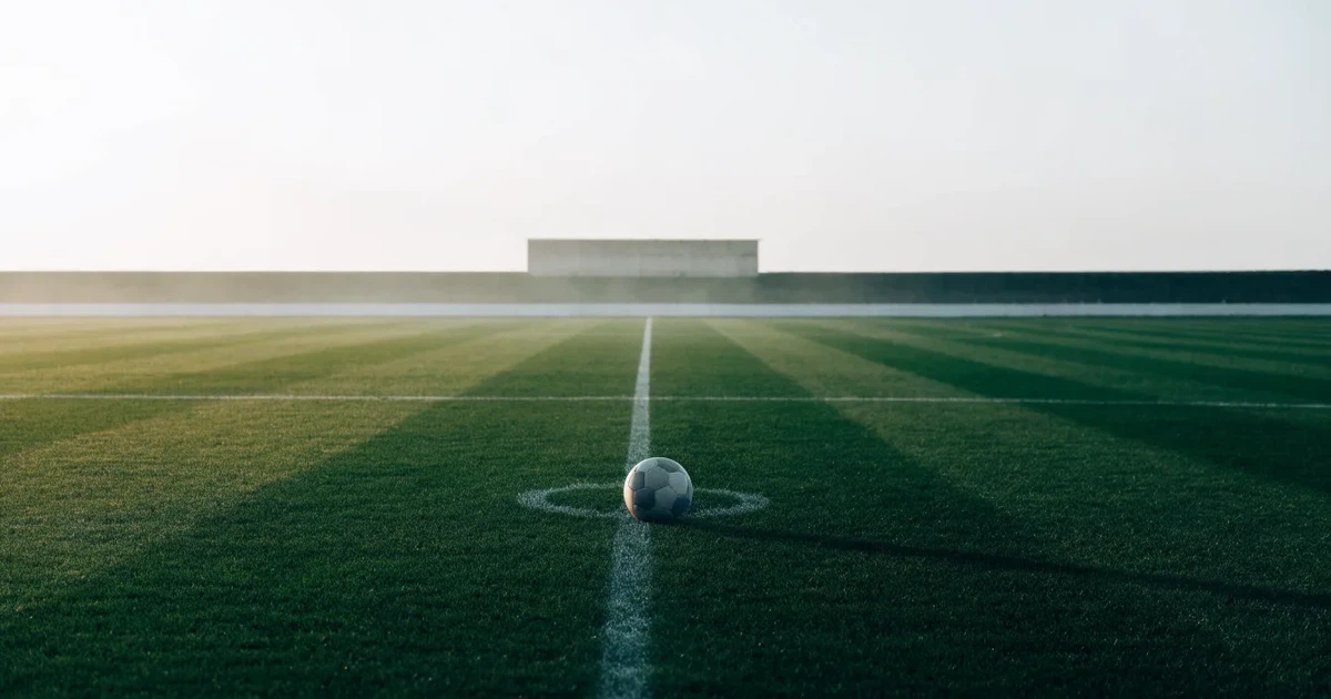 Un pallone da calcio sul dischetto del centrocampo di un prato, alla luce del mattino